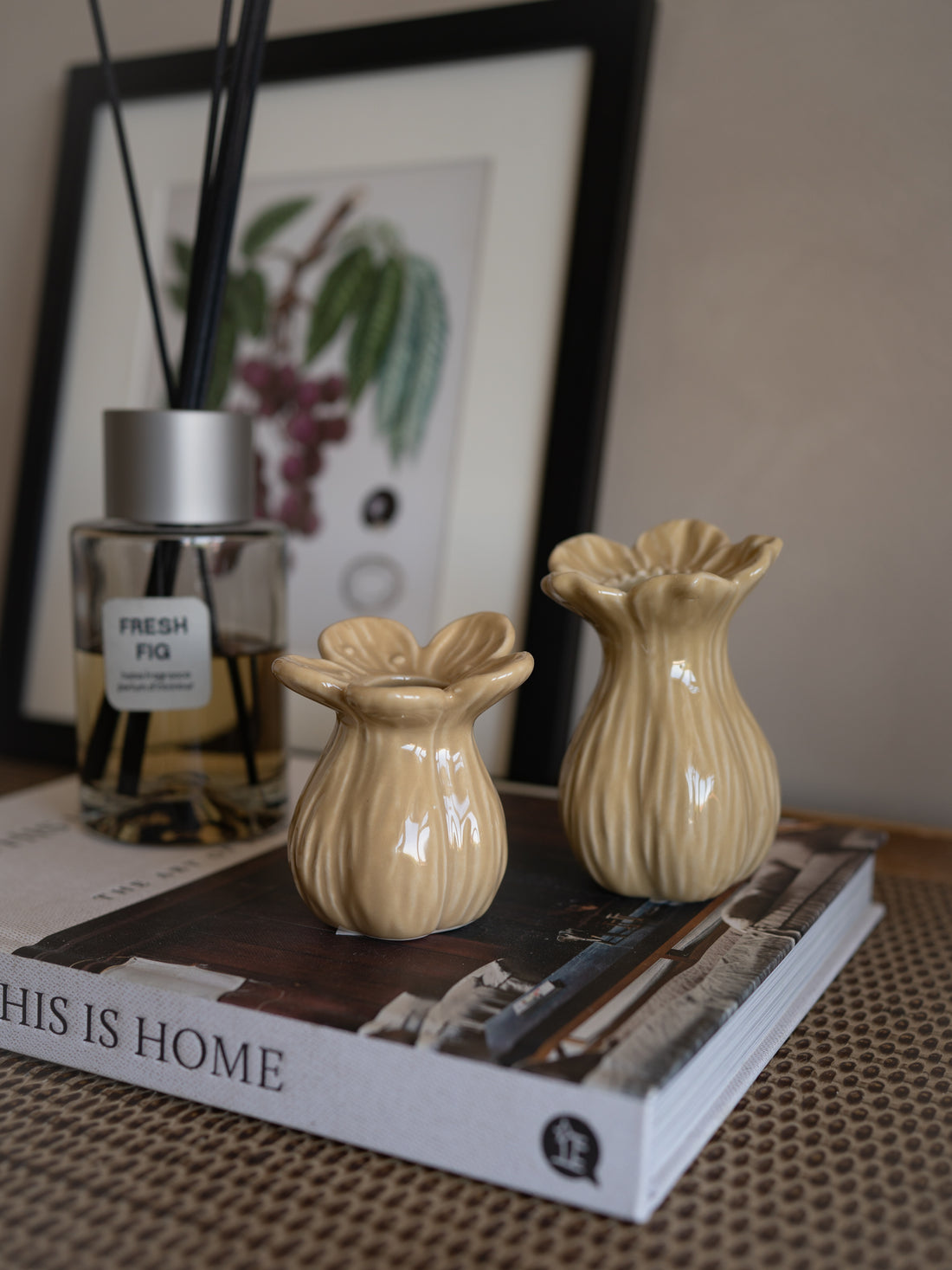 Two beige ceramic petal bud vases on a book with a diffuser bottle in the background.