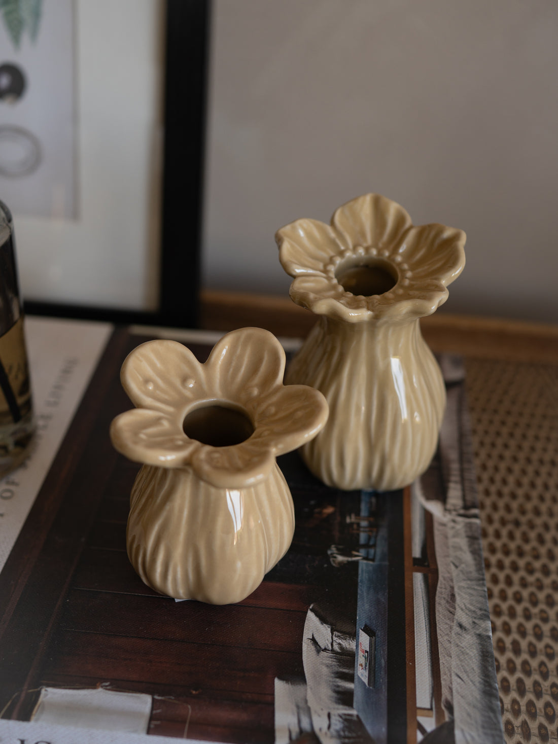 Two beige ceramic flower-shaped vases on a reflective surface with a blurred background.