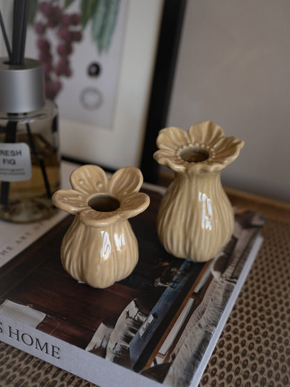 Two beige ceramic flower-shaped bud vases on a magazine with a diffuser and plant in the background.