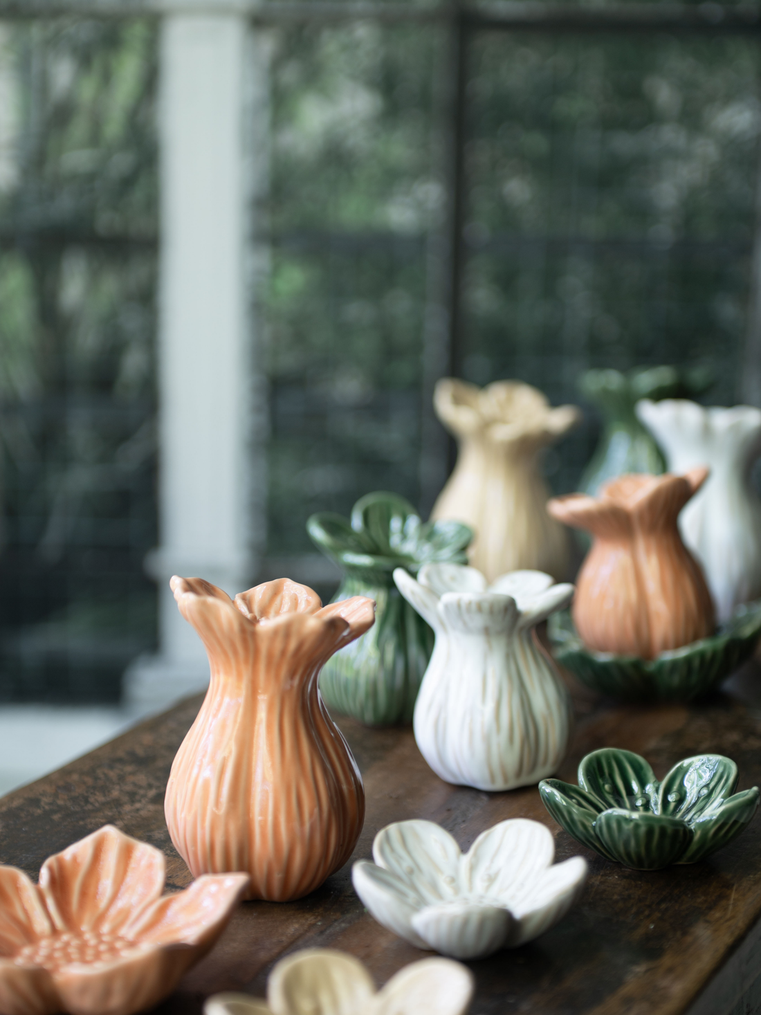Collection of decorative ceramic bud vases on a wooden surface with a blurred greenery background