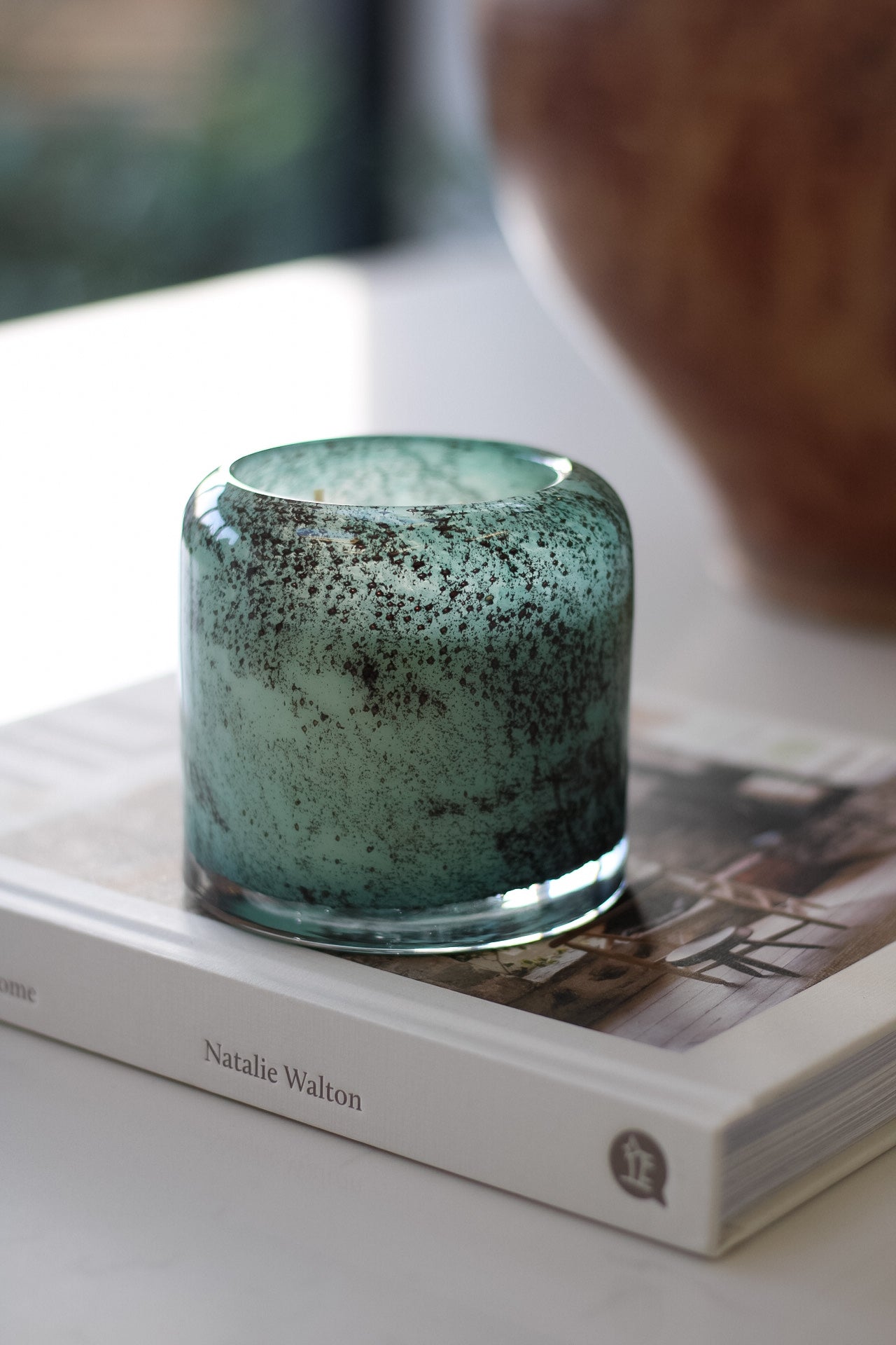 Teal glass candle holder on a book with a blurred background