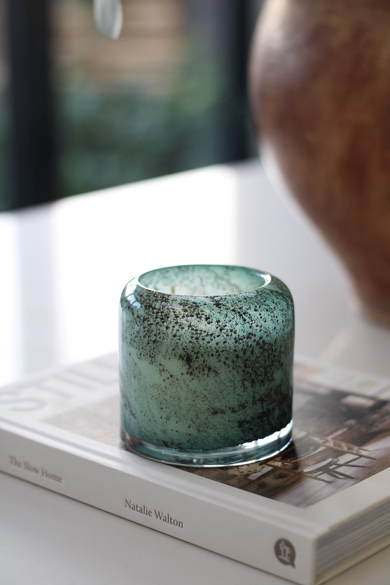 Teal speckled candle on a book with a blurred background