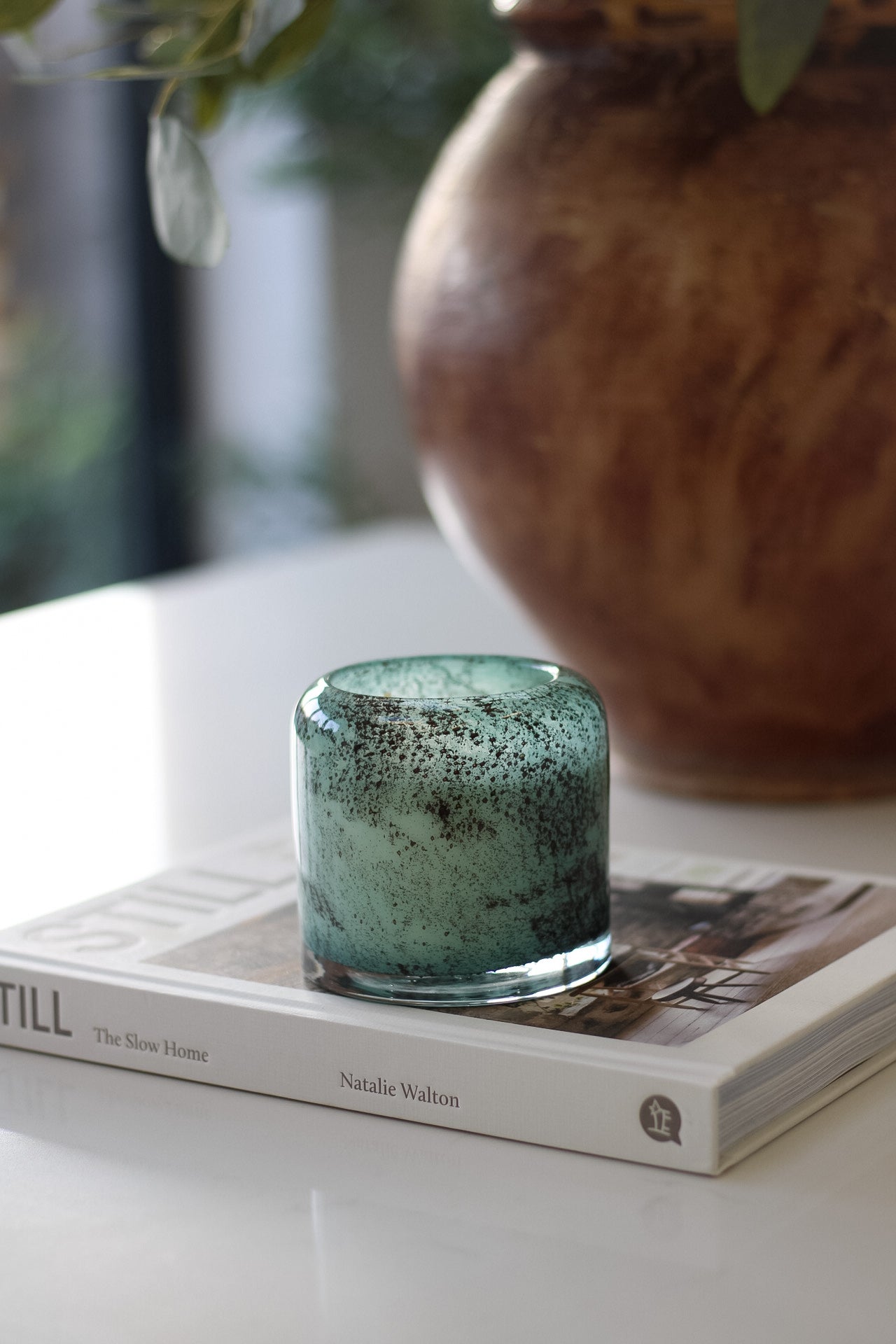 Teal glass candle holder on a book with a blurred vase in the background