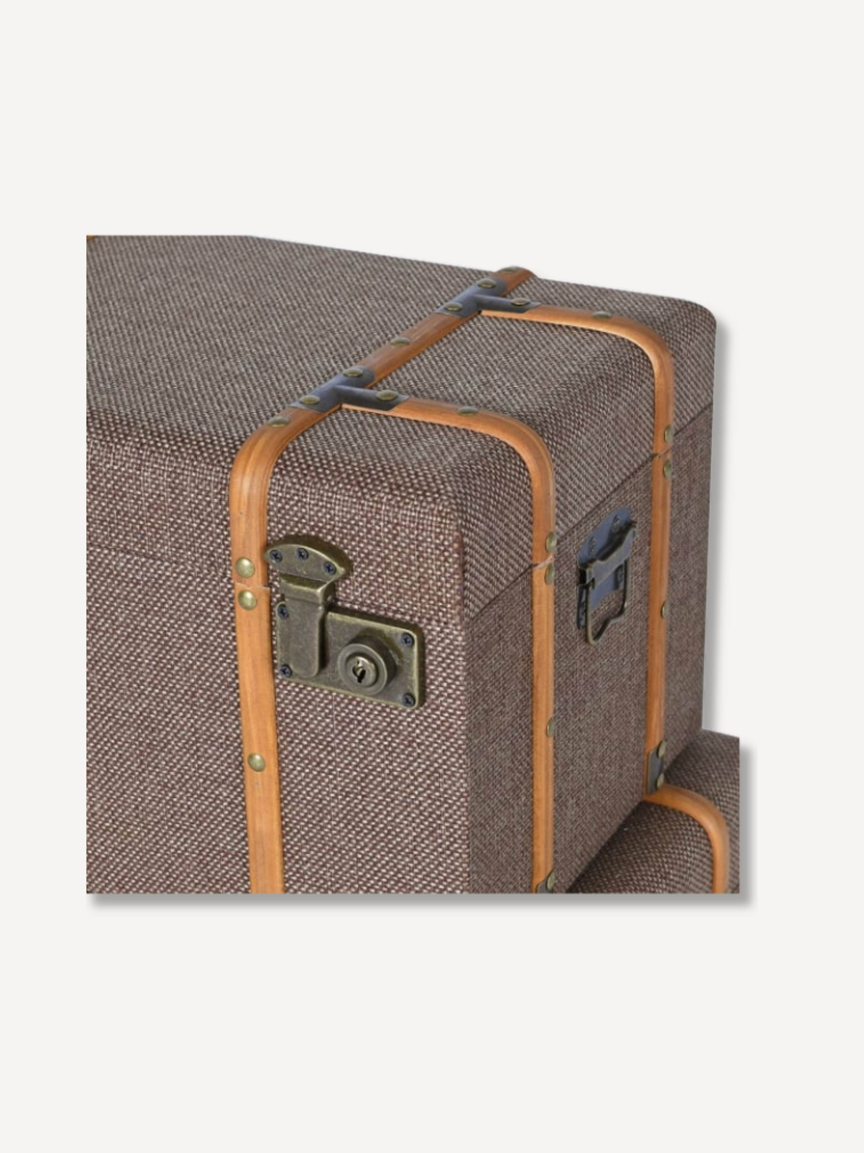 A close-up of a vintage-style trunk or suitcase in brown tweed fabric with tan leather trim and antique metal hardware, shown against a light gray background.