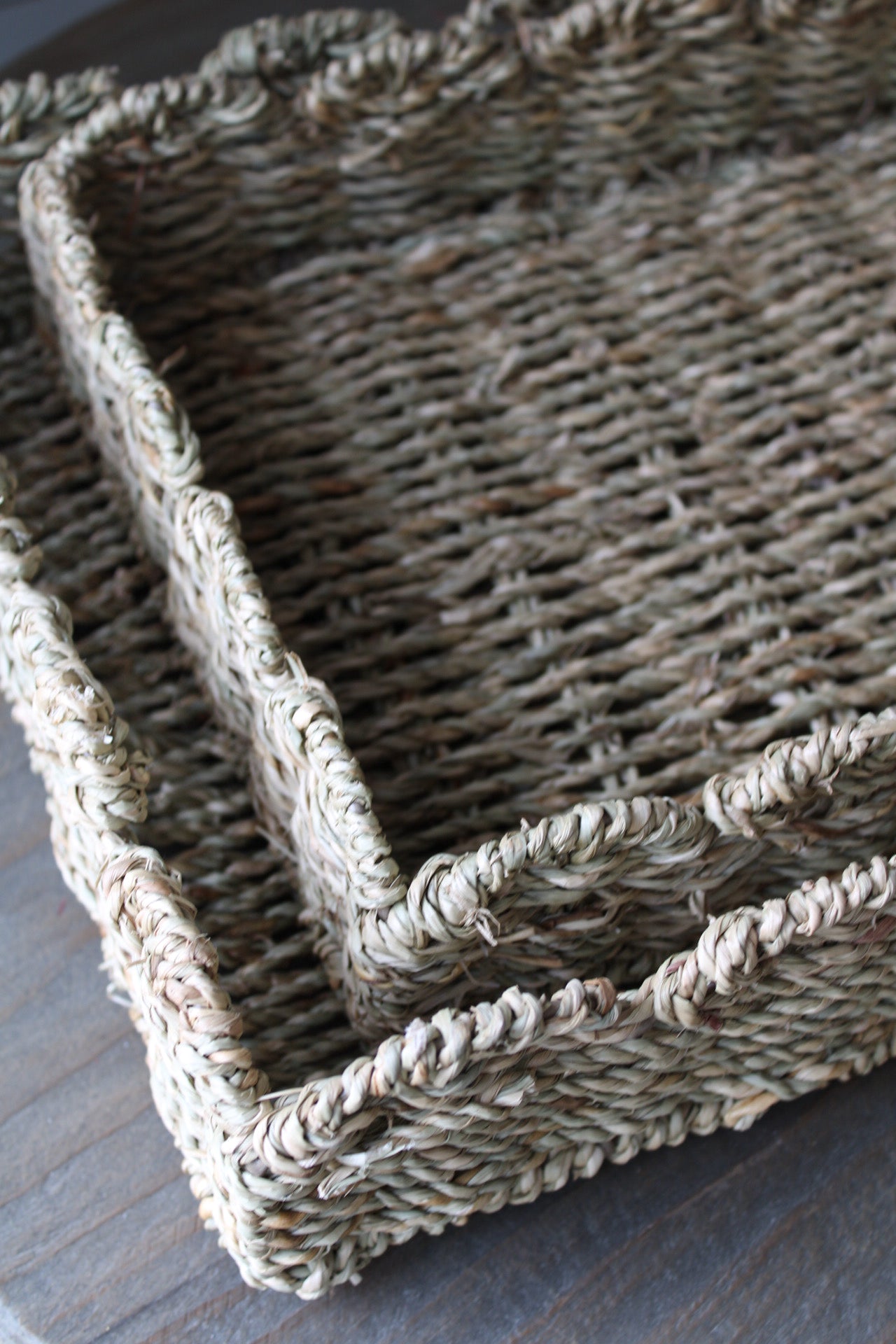 Two scalloped seagrass woven tray on a wooden surface