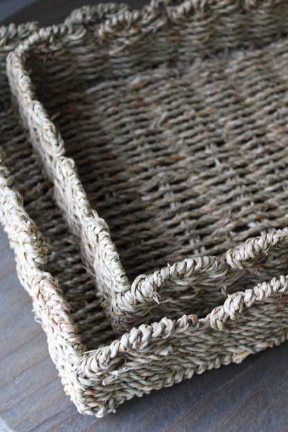 Two scalloped seagrass woven tray on a wooden surface