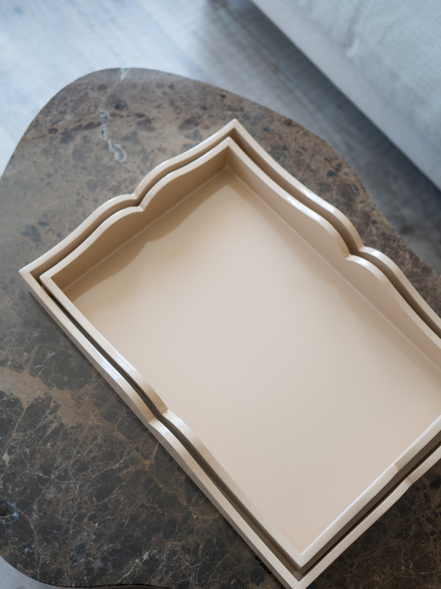 A rectangular beige tray with scalloped edges, nested inside a larger matching tray, displayed on a dark marble surface.