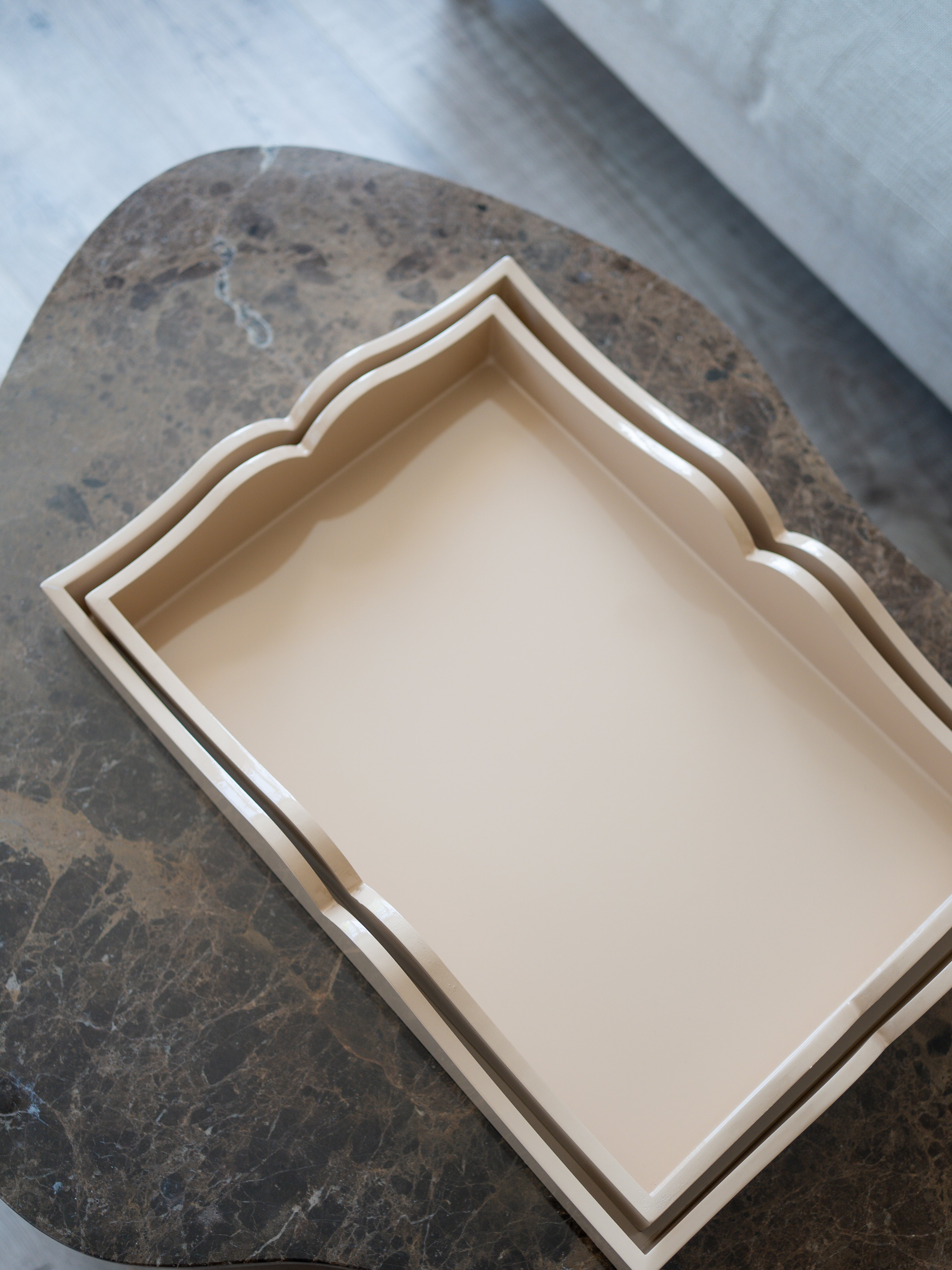 A rectangular beige tray with scalloped edges, nested inside a larger matching tray, displayed on a dark marble surface.