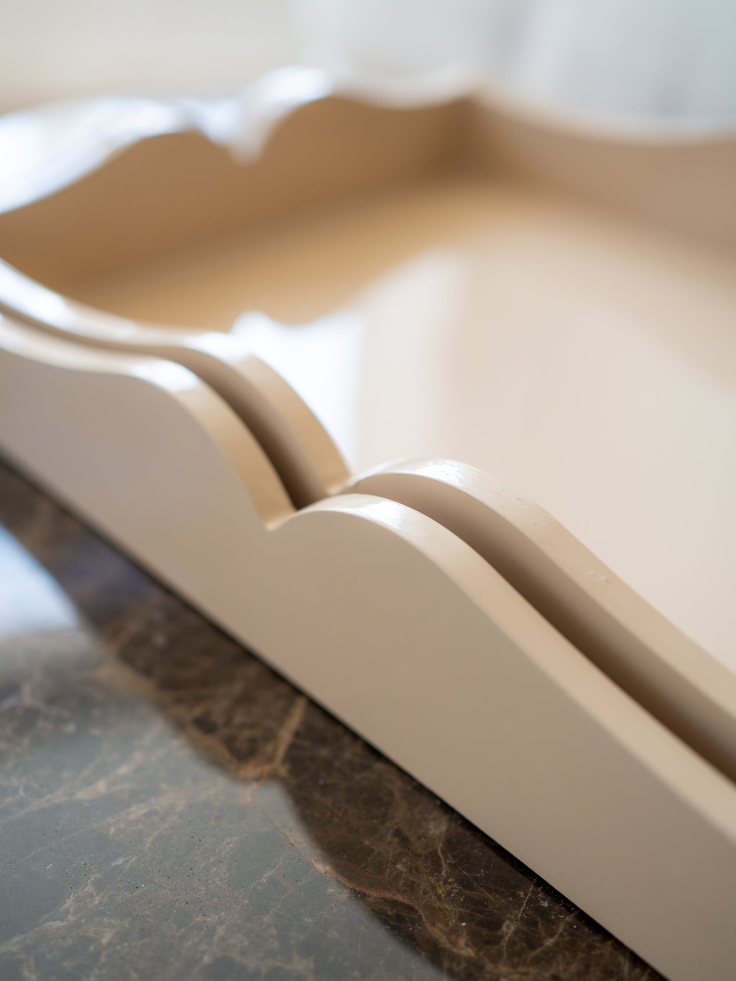 A close-up of a cream-colored wooden tray with scalloped edges, resting on a dark marble surface.