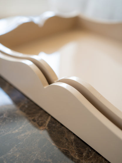A close-up of a cream-colored wooden tray with scalloped edges, resting on a dark marble surface.