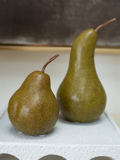 Two whole pears with brown stems, one smaller and one larger, standing on a white textured surface against a neutral background.