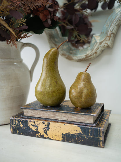 Two decorative pears with a rustic, distressed glaze sit on top of two vintage-style books. The books feature a dark navy blue and gold map design.