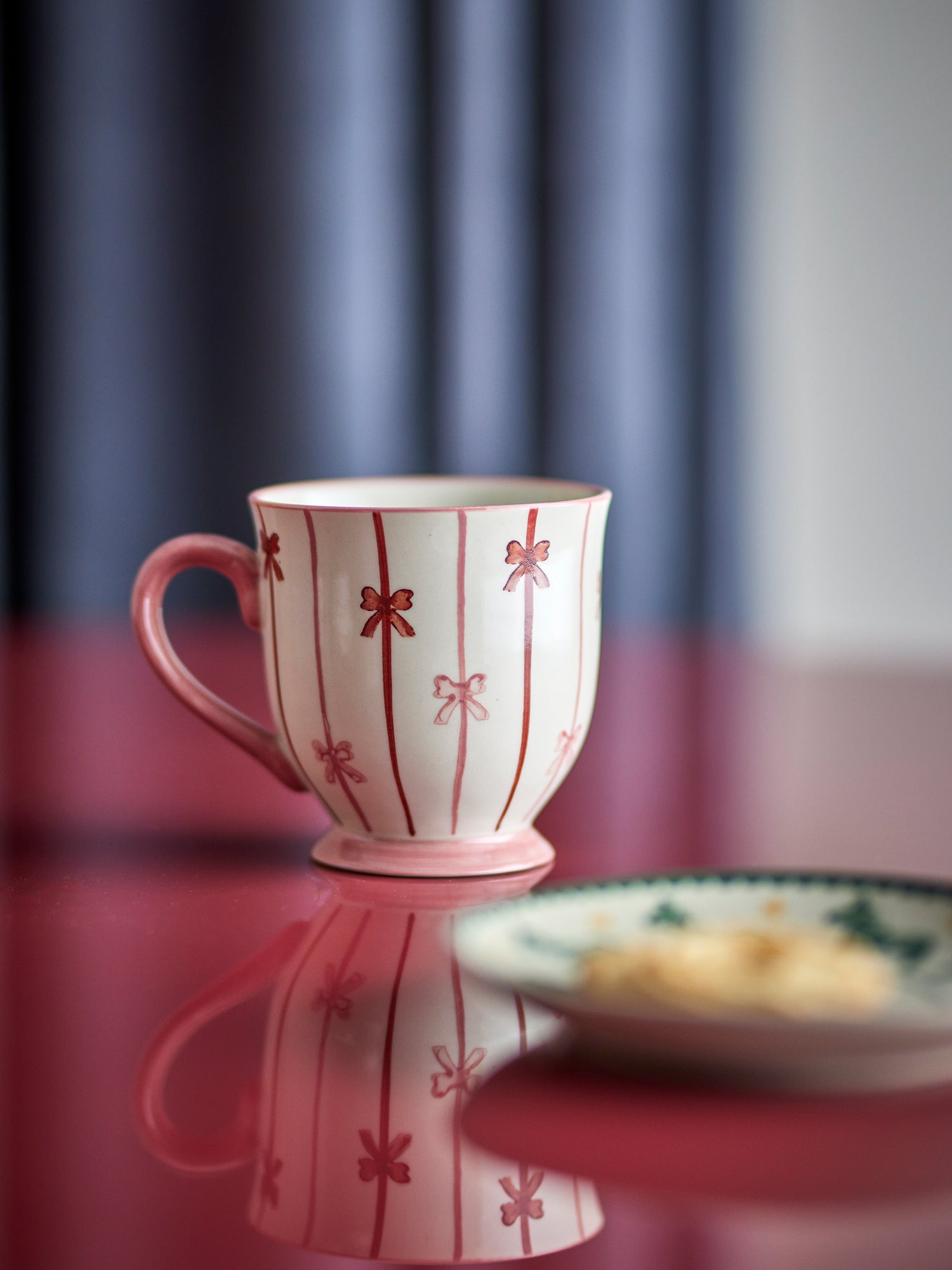 Pink mug with red floral patterns on a reflective surface with a blurred background