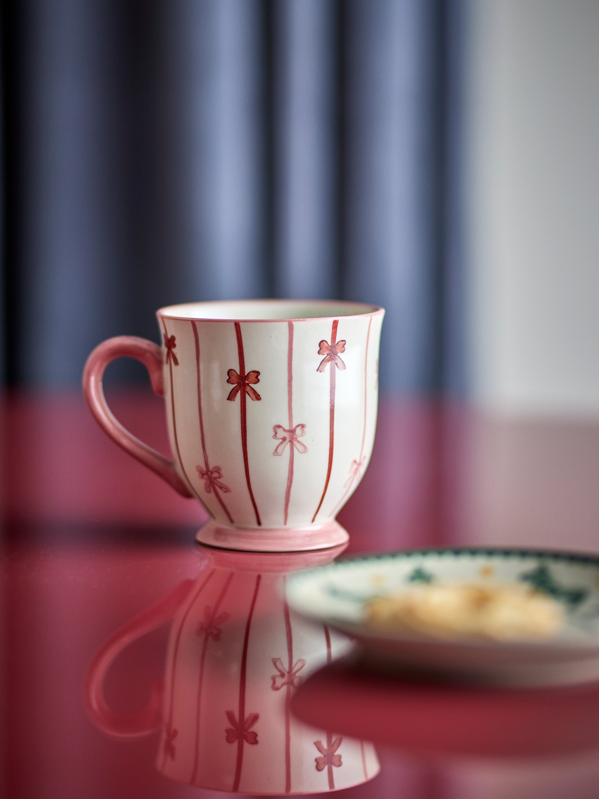 Pink mug with red floral patterns on a reflective surface with a blurred background