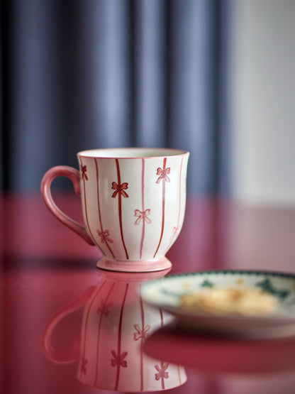Pink mug with red floral patterns on a reflective surface with a blurred background