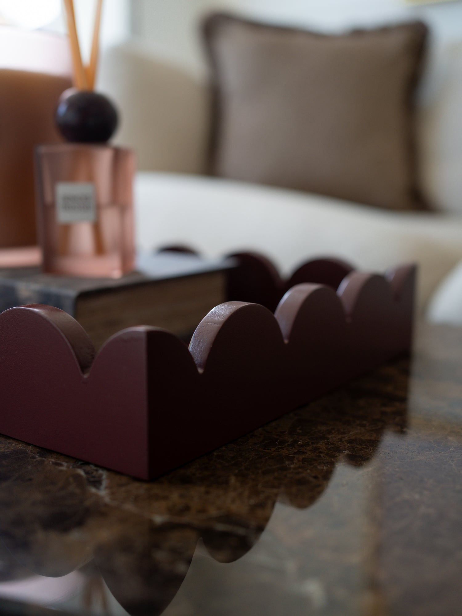 A dark burgundy scalloped tray or organizer placed on a polished dark marble table in a softly blurred living room setting.
