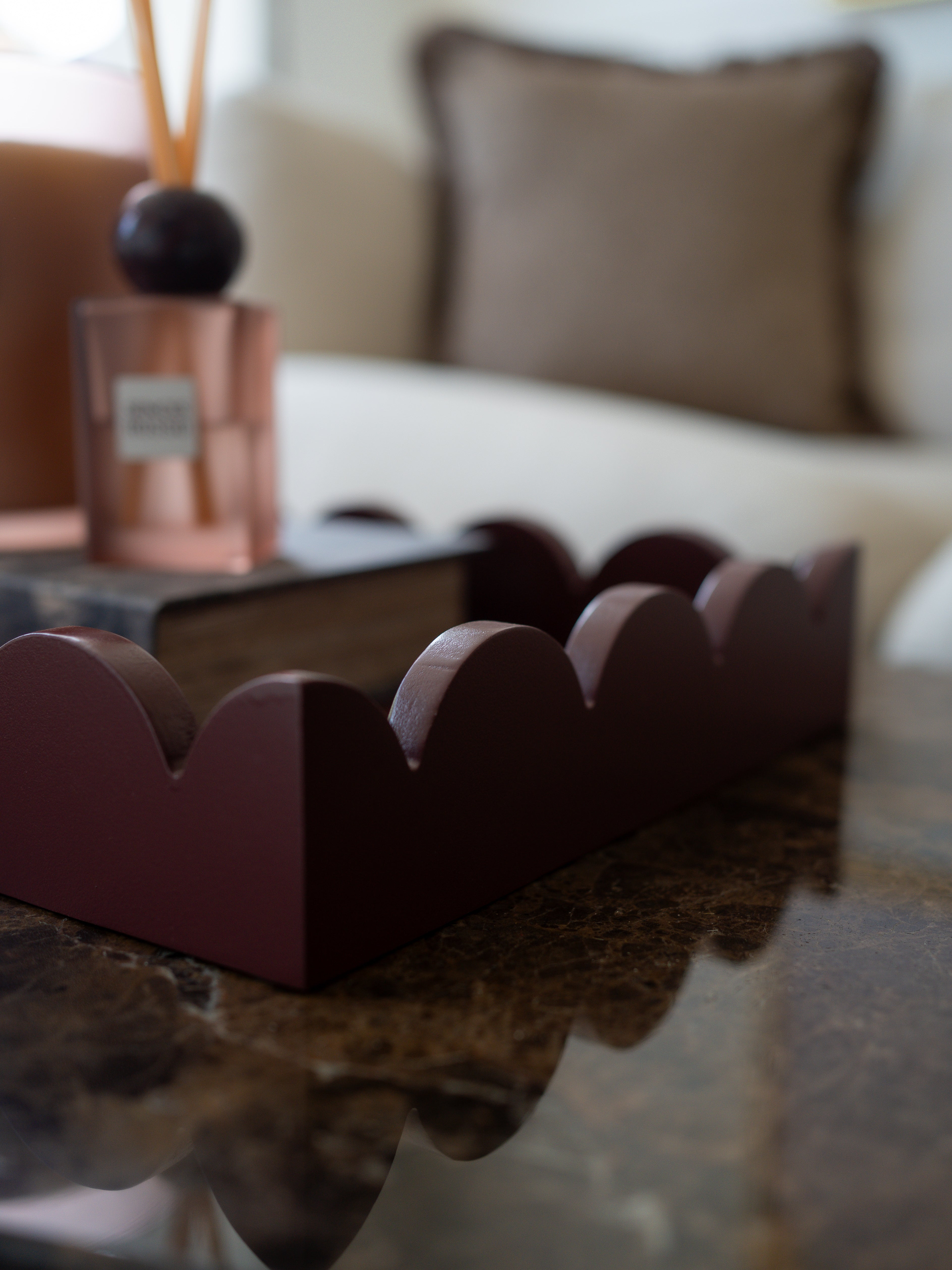 A dark burgundy scalloped tray or organizer placed on a polished dark marble table in a softly blurred living room setting.