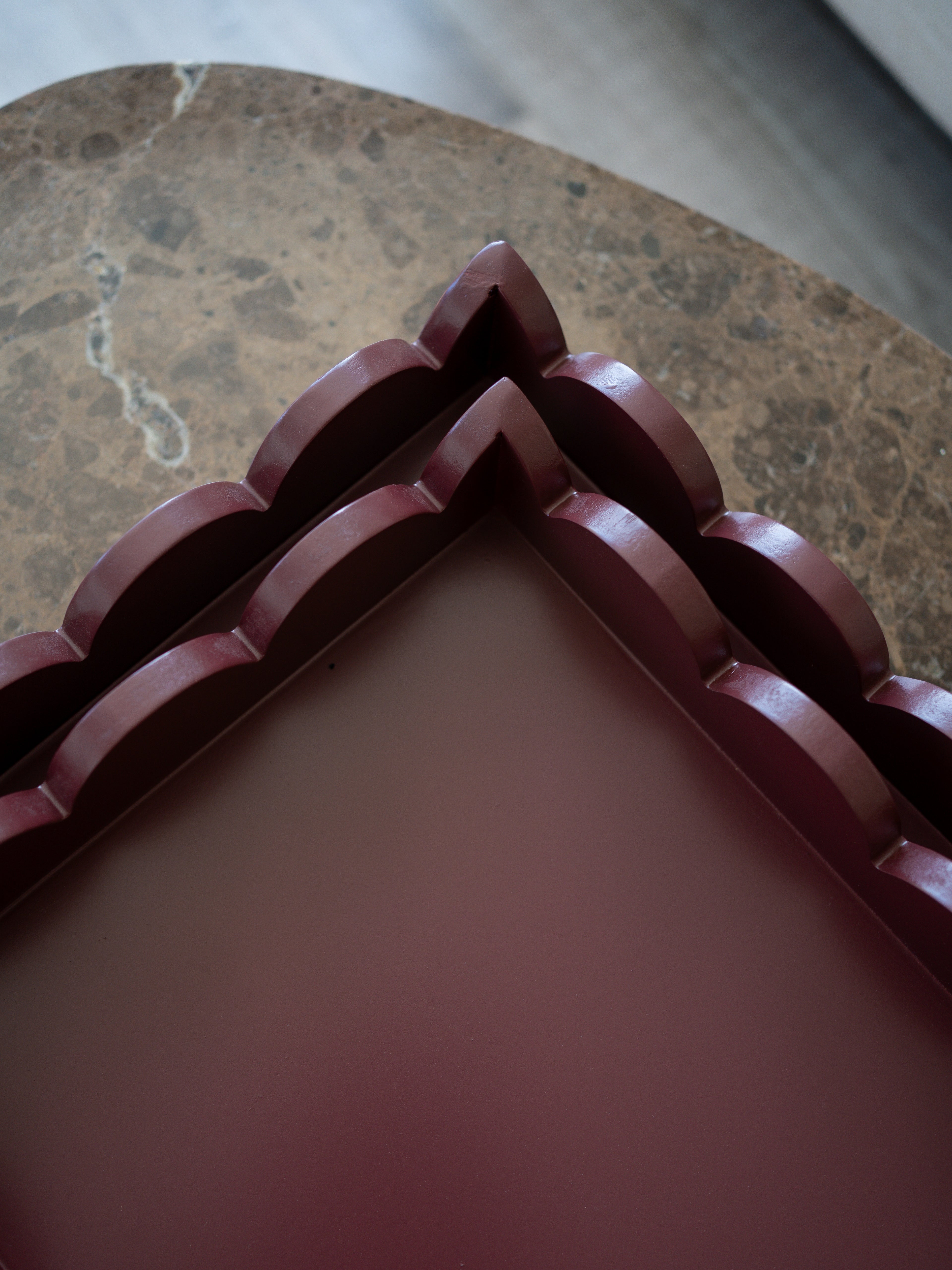 A close-up of a dark reddish-brown decorative tray or box corner with layered scalloped edges, placed on a brown marble surface.