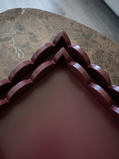 A close-up of a dark reddish-brown decorative tray or box corner with layered scalloped edges, placed on a brown marble surface.