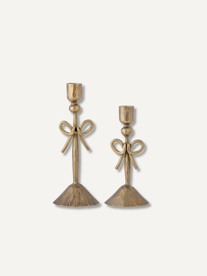 A pair of vintage-style brass candlesticks with bow details and flared bases, displayed on a clean off-white background.