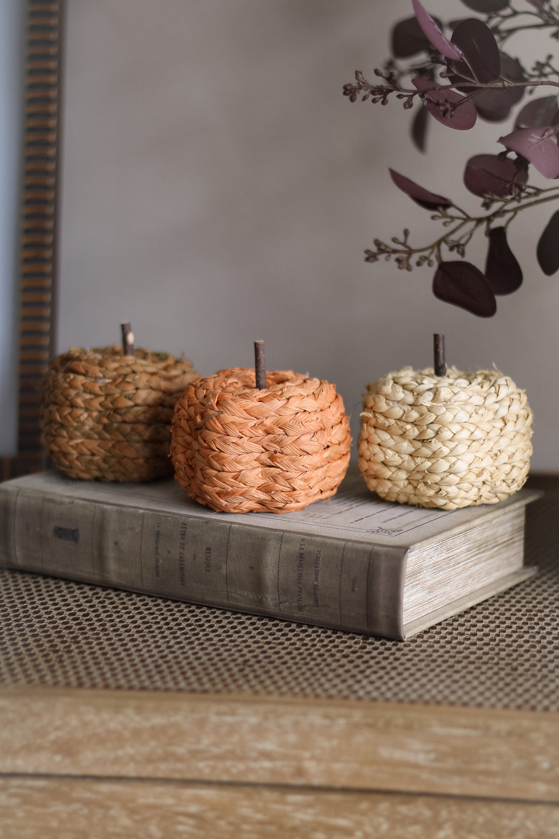 Three woven pumpkins on a wooden surface with a blurred background