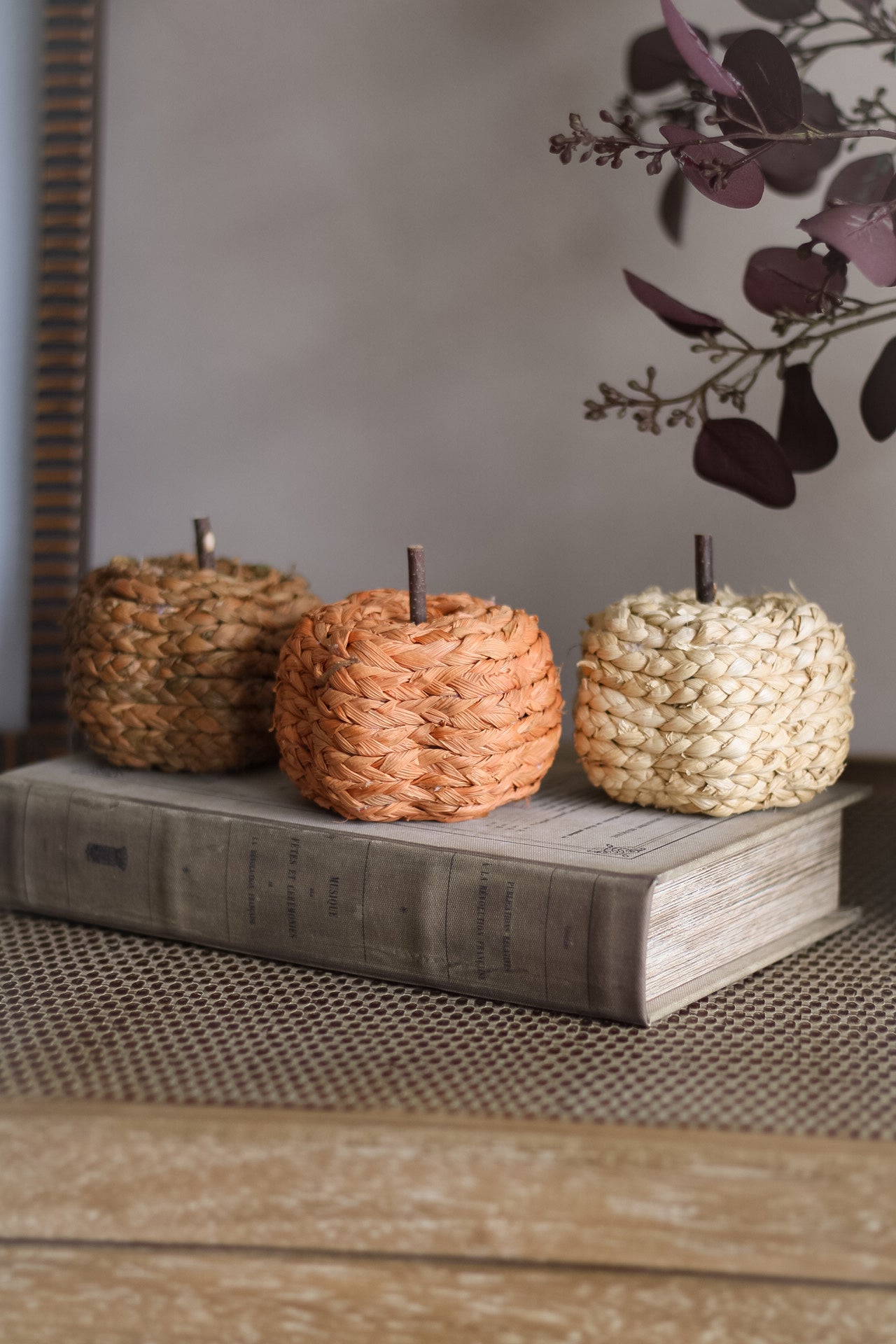 Three woven pumpkins on a wooden surface with a blurred background