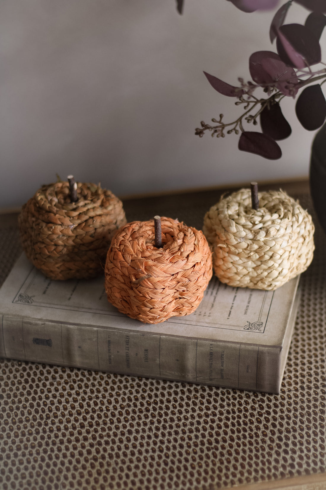 Three woven decorative pumpkins on a textured surface with a blurred background