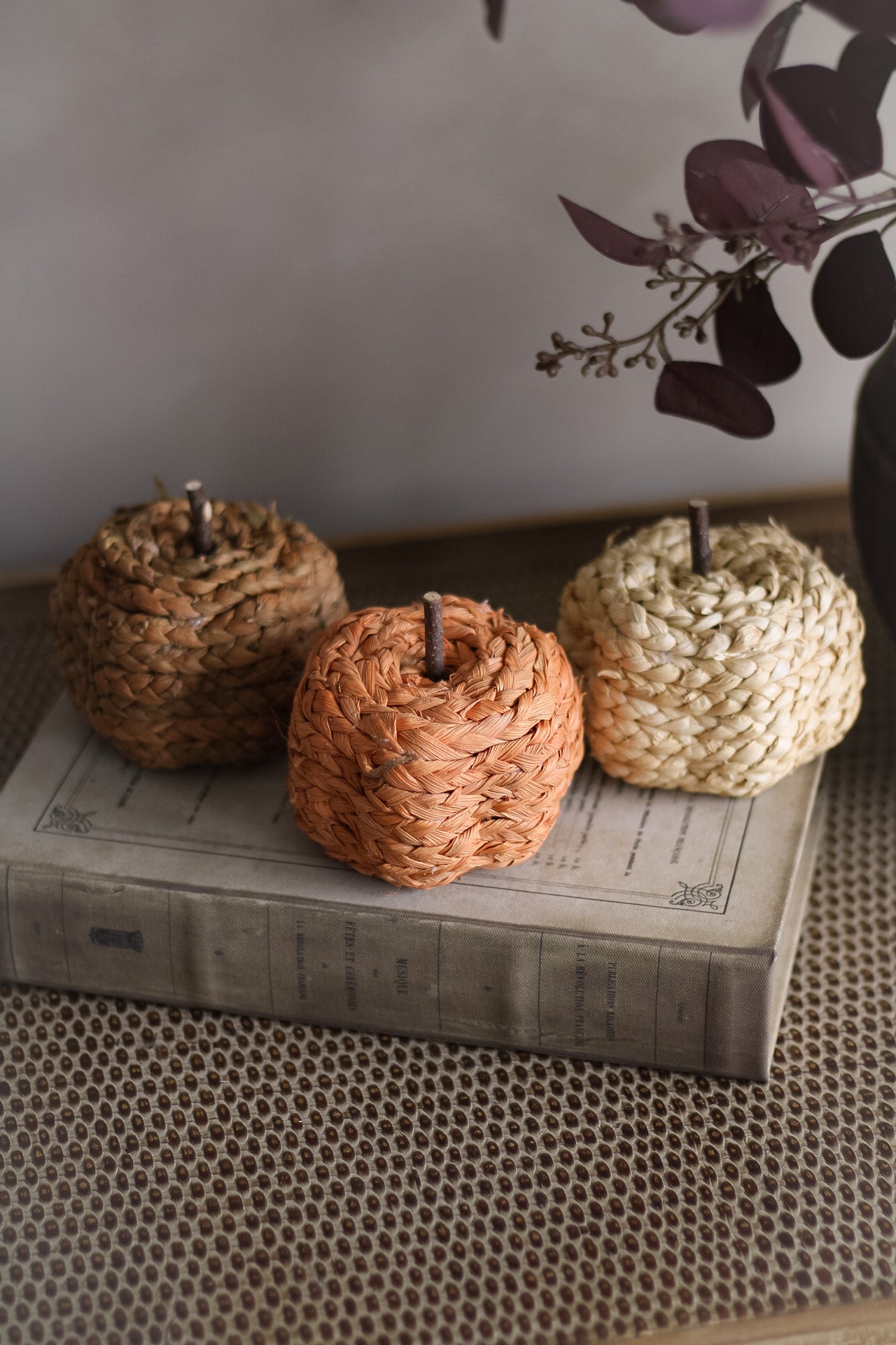 Three woven decorative pumpkins on a textured surface with a blurred background