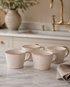 Set of four beige ceramic mugs on a marble countertop with a kitchen background.