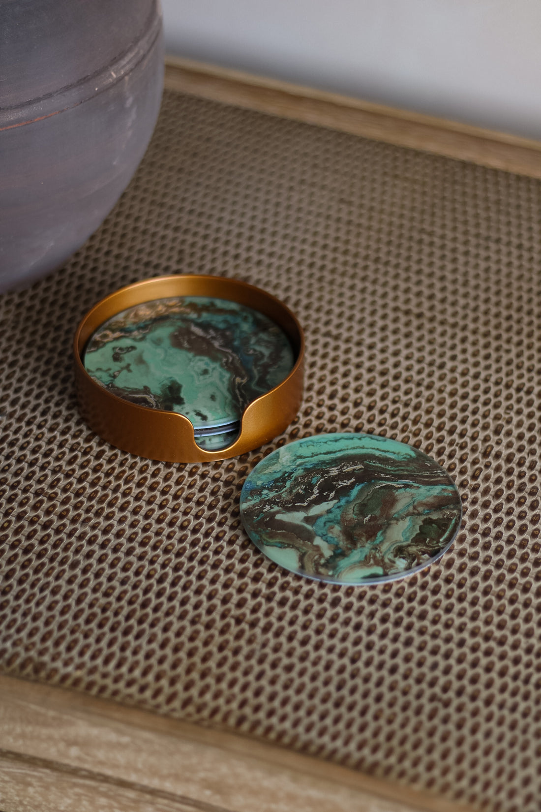 Two green marbled stones with gold rimmed container on textured surface
