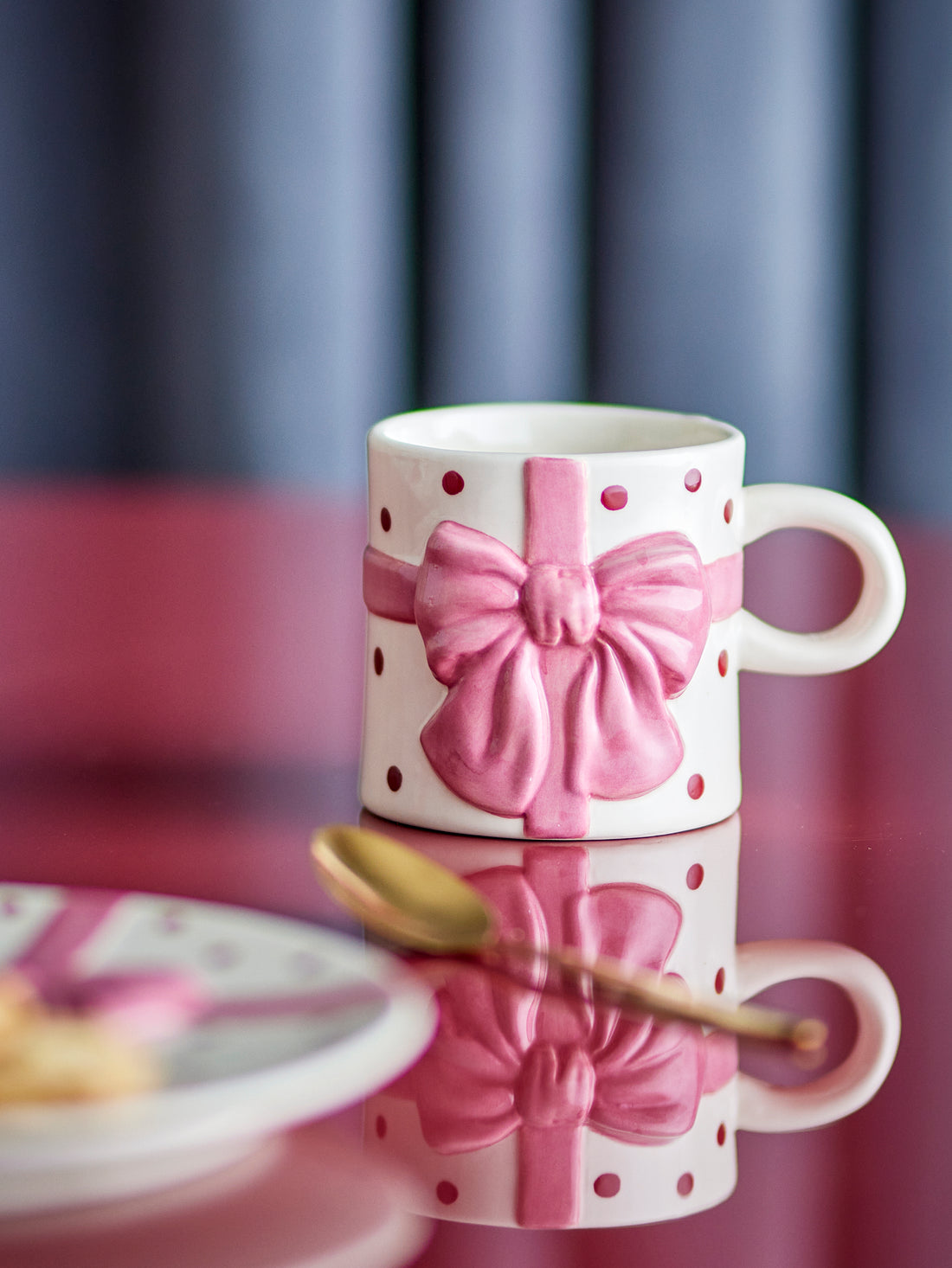 White mug with pink bow design on a reflective surface