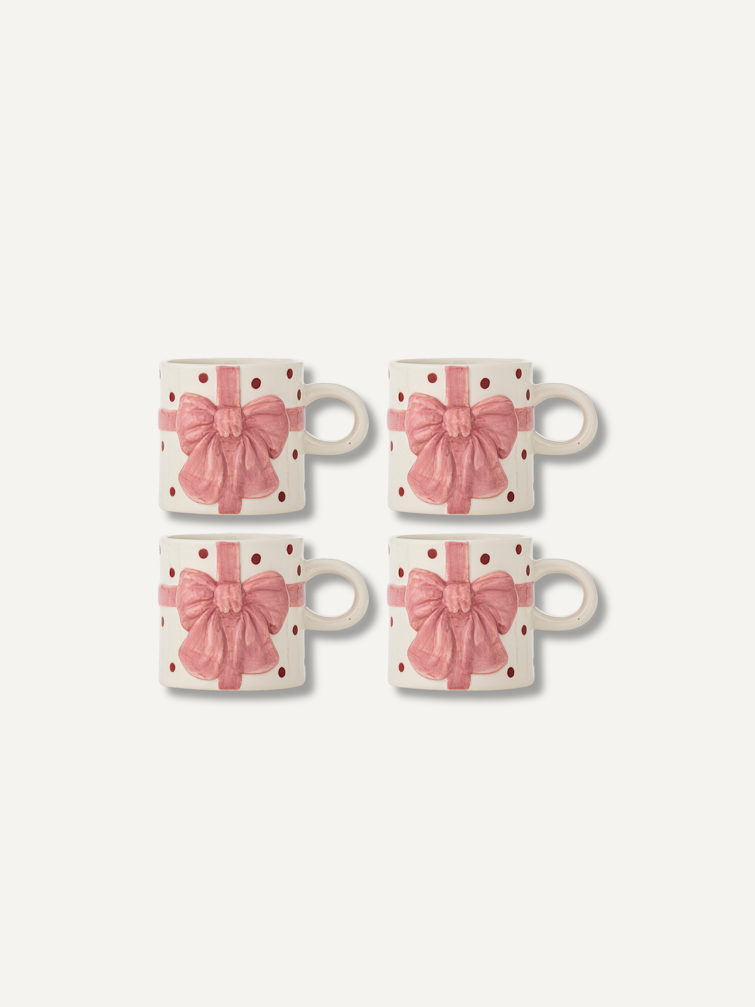 Four white ceramic mugs with pink gift bow and polka dot patterns, arranged in a 2x2 grid on a light off-white background.