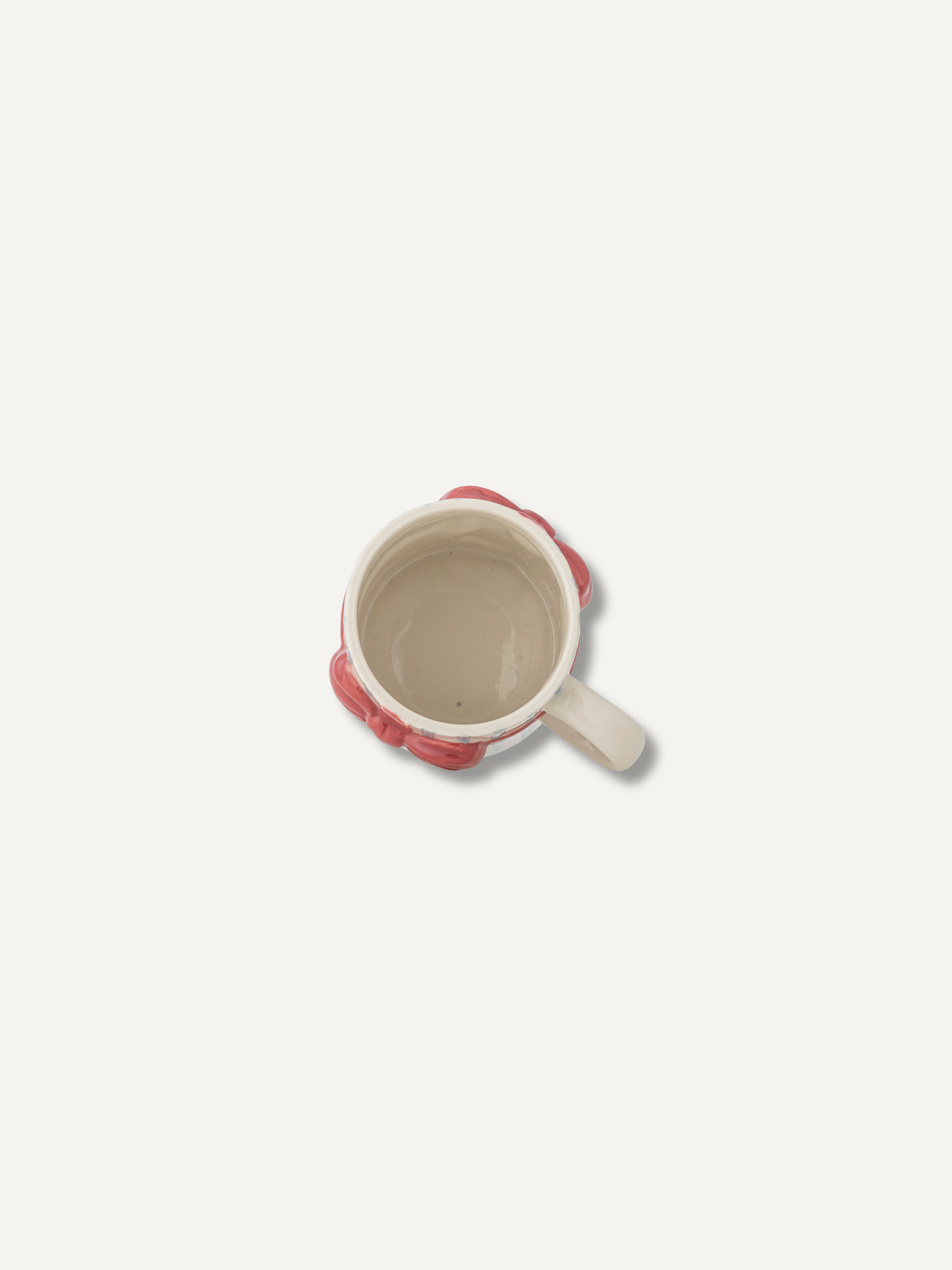 A top-down view of a ceramic mug with a cream-colored interior and handle, featuring a textured, raised pinkish-red exterior border.