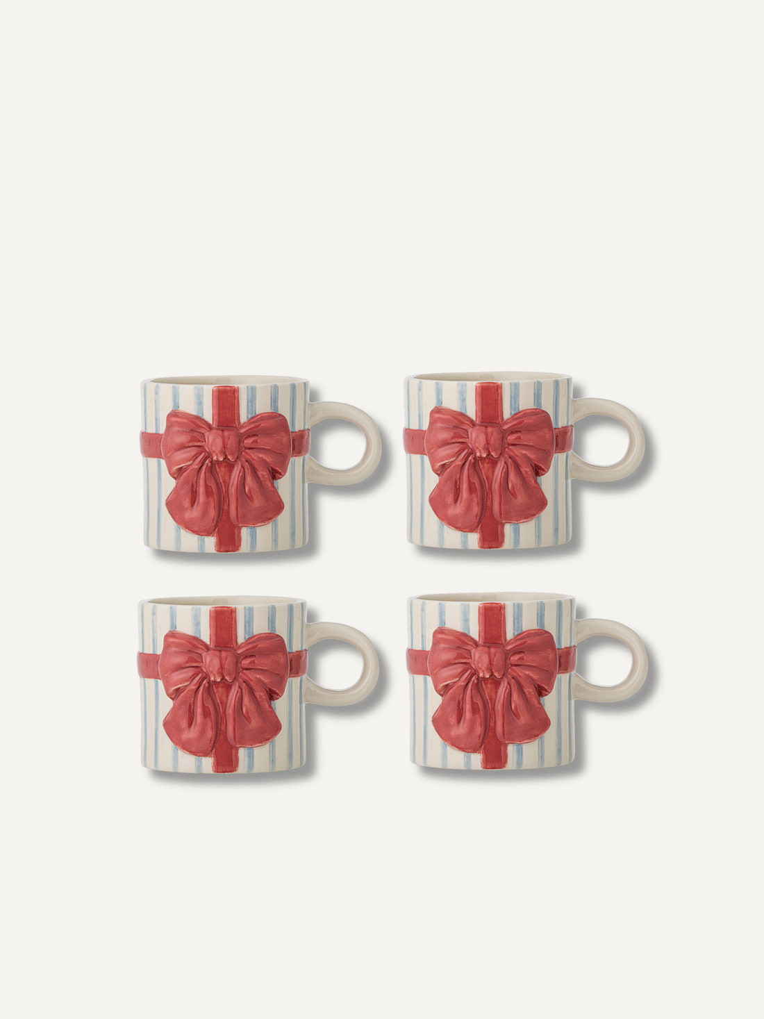Four ceramic mugs arranged in a 2x2 grid, each decorated with a red gift bow and ribbon motif over a white and pale blue striped background, on a light off-white backdrop.