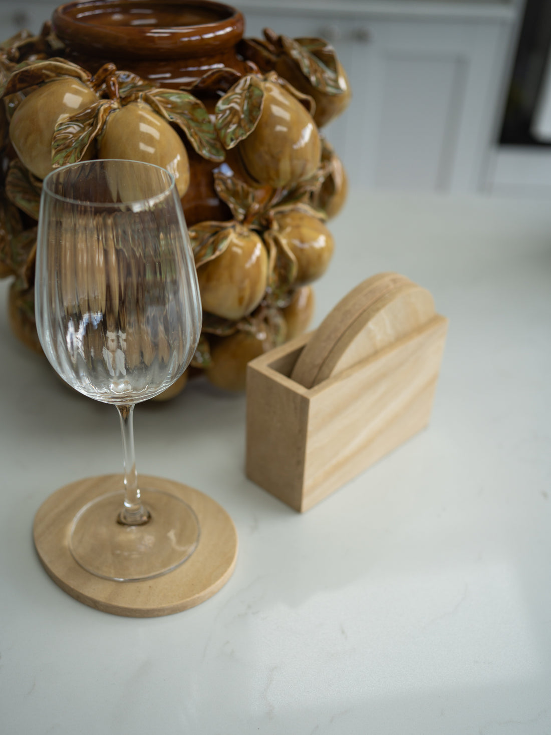 Wine glass on a travertine effect coaster with a decorative ceramic item in the background.