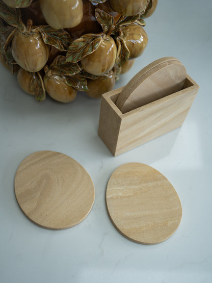 Travertine effect coasters and holder on a light surface with a ceramic pear vase in the background.
