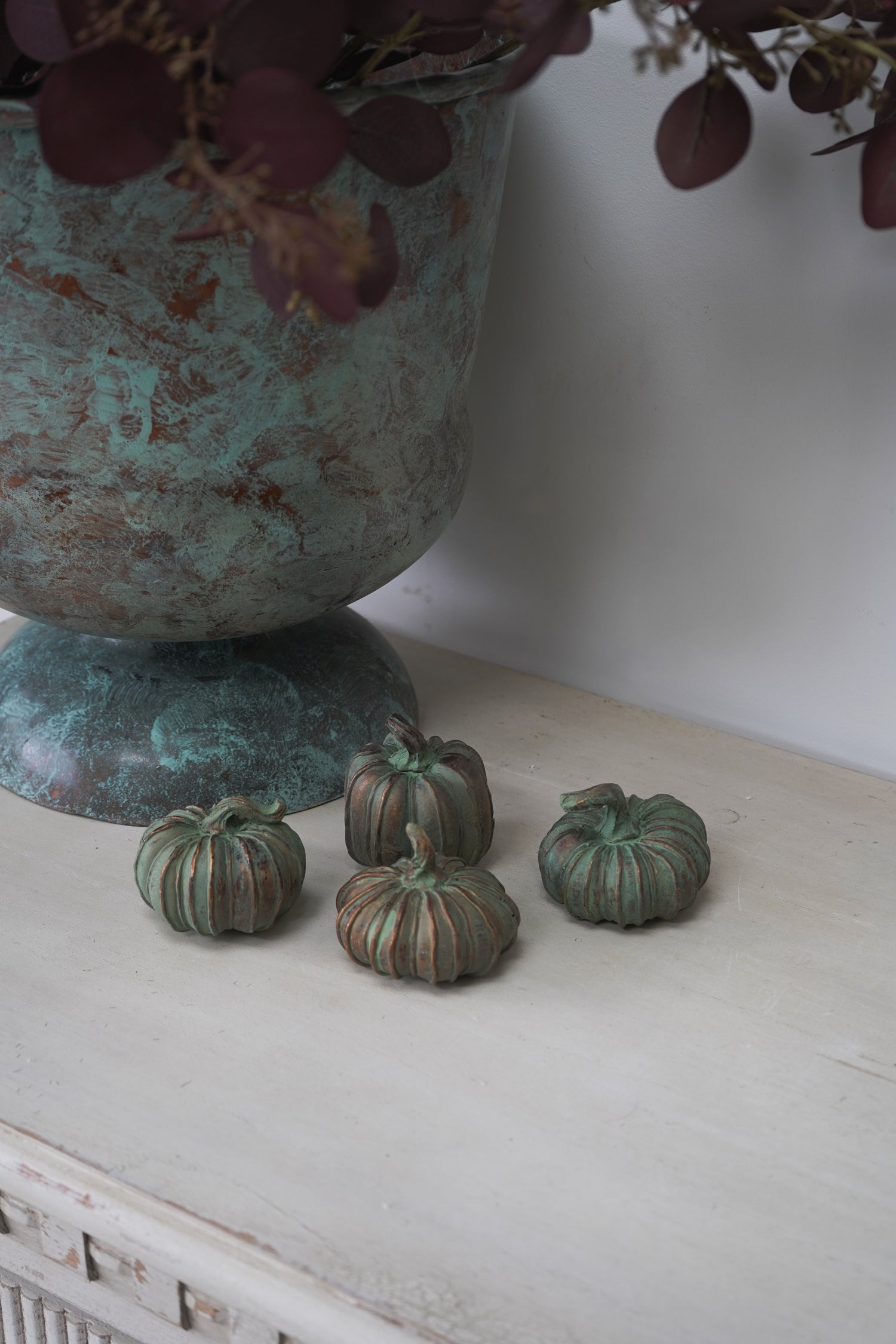 Small green pumpkins on a white surface with a textured vase in the background