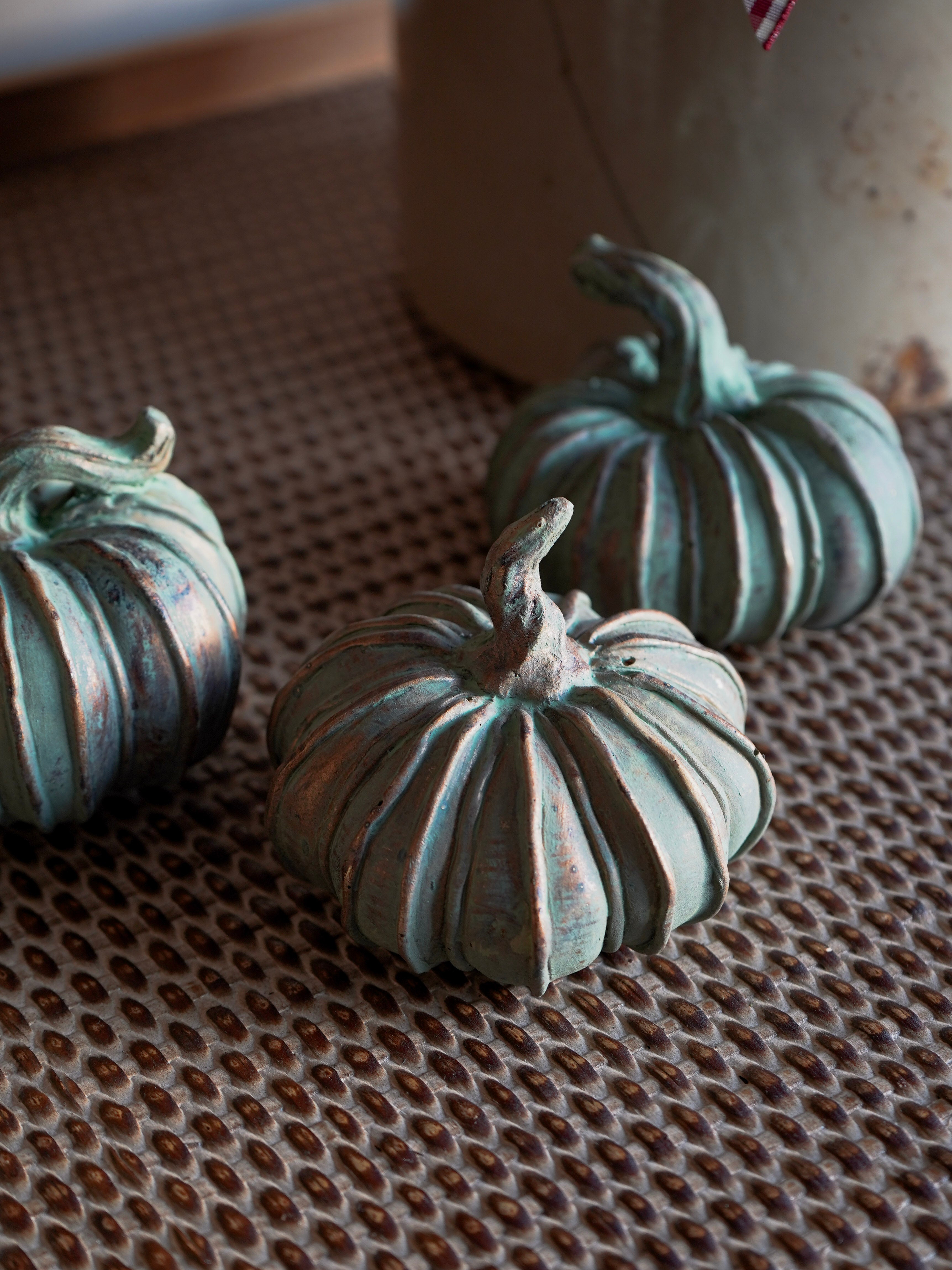Three decorative pumpkins with a textured surface on a woven mat.