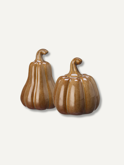 Two glossy ceramic pumpkins in brown and tan glaze, standing on a light off-white background.
