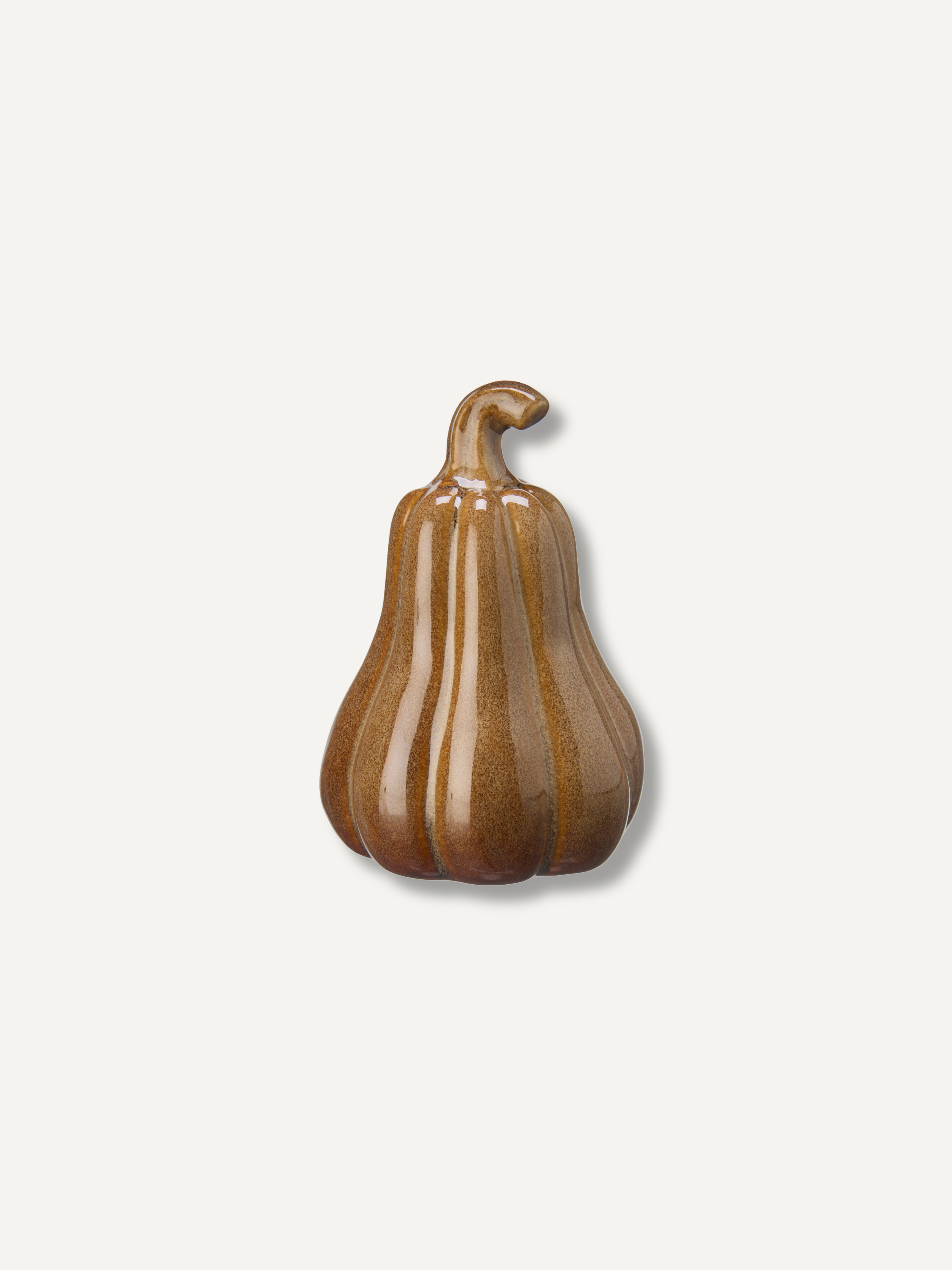 A small decorative ceramic pumpkin figurine with a glossy brown and amber glaze, set against a solid off-white background.