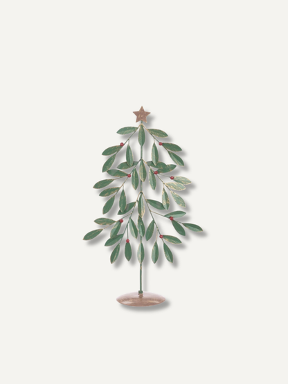 A decorative metal tree ornament with green leaves, small red berries, and a gold star on a light beige background.