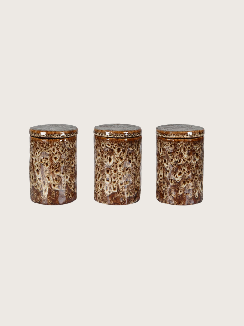 Three ceramic jars with a speckled glaze on a beige background