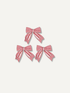 Three red and white striped fabric christmas bows arranged in a pyramid on a light beige background.