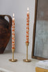 Two tall candles with pumpkin patterns in gold candle holders on a surface.