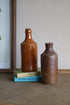 Two brown ceramic bottles on a textured surface with a book in the background.