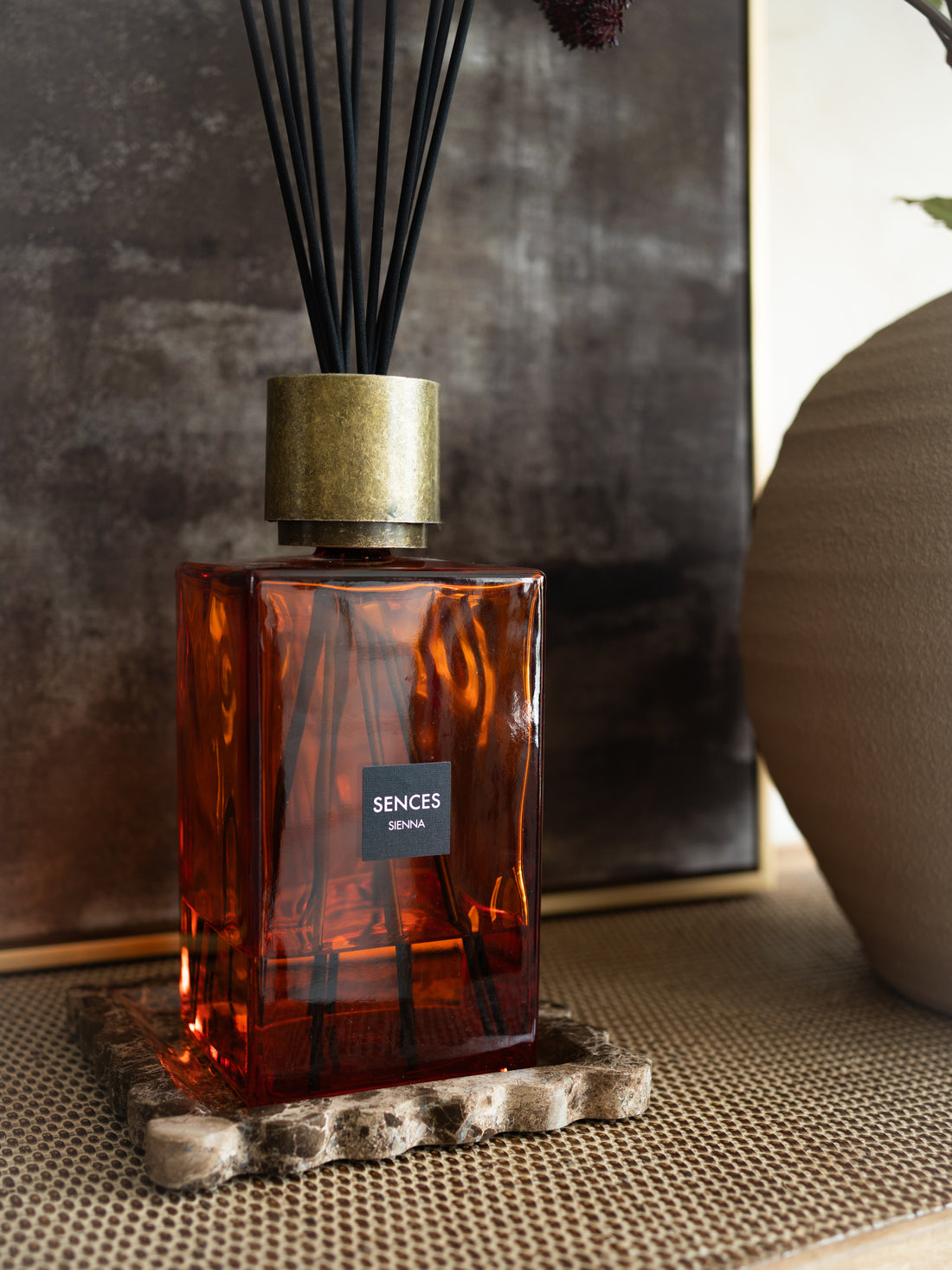 Orange glass Sienna statement luxury reed diffuser bottle with gold cap on a textured surface