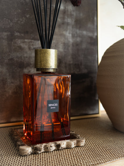 Orange glass Sienna statement luxury reed diffuser bottle with gold cap on a textured surface