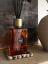 Orange glass Sienna statement luxury reed diffuser bottle with gold cap on a textured surface