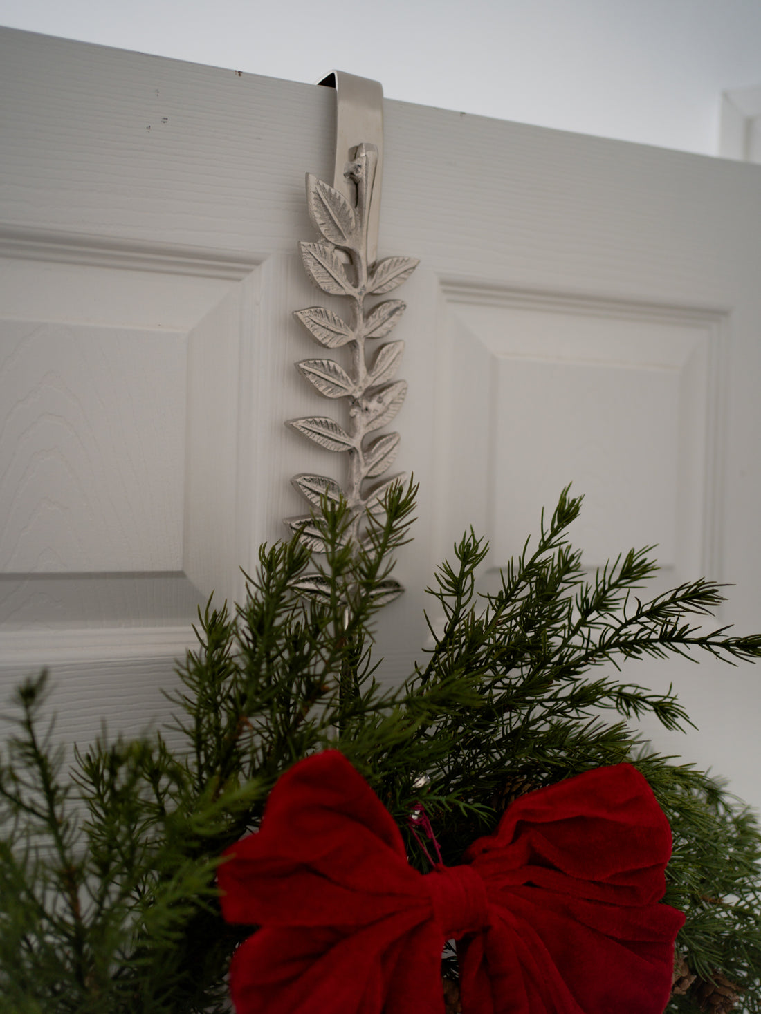 Decorative wreath with a red bow and leaf design on a white door