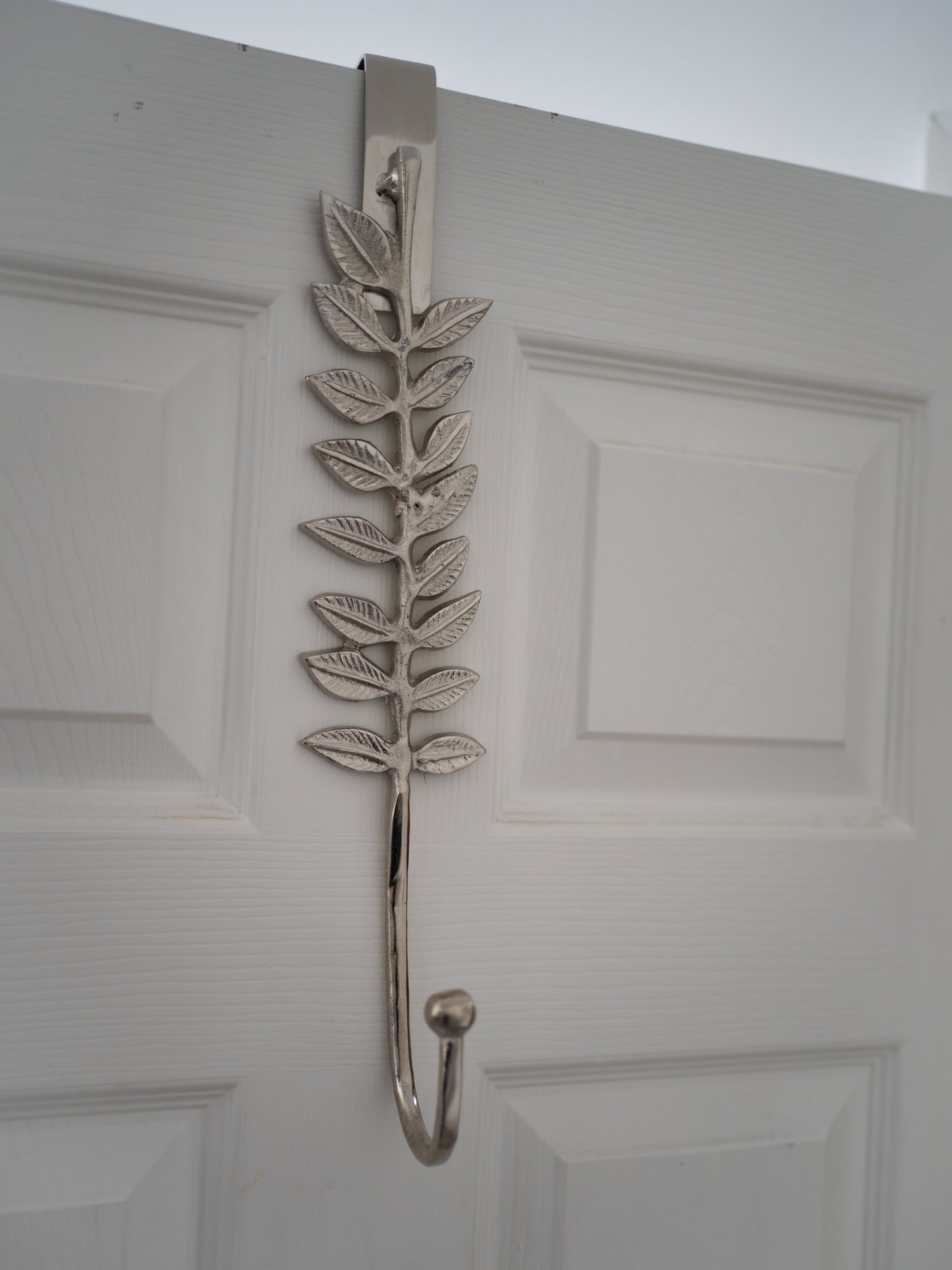 Decorative leaf-shaped wreath hanger on a white door